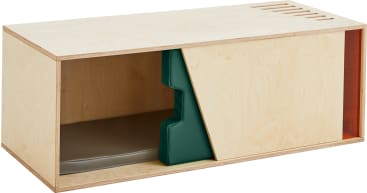 Eine rechteckige Holzkiste mit offener Vorderseite, einer grünen stufenförmigen Trennwand, einer Schiebetür aus hellem Holz und einer grauen gepolsterten Matte im Inneren. Die Kiste hat Lüftungsschlitze in der rechten oberen Ecke.
