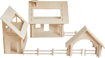Drei unfertige Miniaturgebäude aus Holz sind durch einen einfachen Holzzaun und ein Tor miteinander verbunden. Jedes Gebäude hat ein offenes Dach oder Fenster, und das Holz hat eine helle, natürliche Oberfläche.