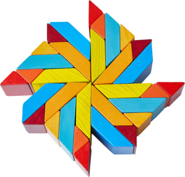 Geometrische Anordnung von bunten Holzklötzen, darunter Dreiecke und Parallelogramme, die ein symmetrisches Sternmuster mit roten, gelben, blauen und orangen Teilen bilden.