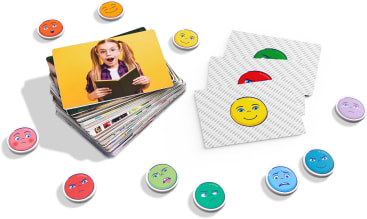 Ein Kartenstapel mit einer Karte, die ein überraschtes Mädchen mit einem Buch in der Hand zeigt, drei verdeckte Karten mit Smiley-Gesichtern und mehrere runde Spielsteine mit verschiedenen Gesichtsausdrücken umgeben die Karten.