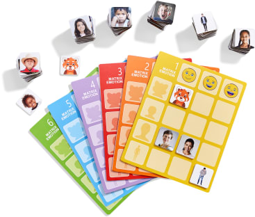 Sechs farbenfrohe Spielbretter mit der Aufschrift "Matrix Emotion" und ausgeschnittenen Feldern sind ausgelegt, über denen jeweils entsprechende Bildplättchen liegen, die menschliche Gesichter und Zeichentrickfiguren zeigen, die verschiedene Emotionen ausdrücken.