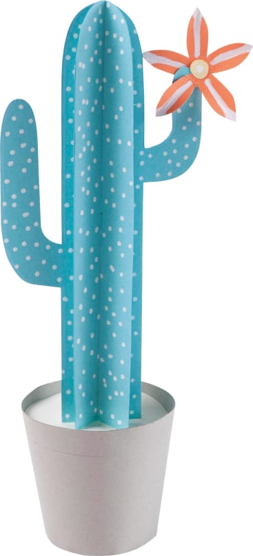Ein Papierkaktus mit blau-grünen Armen und weißen Punkten steht in einem schlichten weißen Topf. Ein Arm hält eine orangefarbene und weiße Papierblume in der Nähe der Spitze.