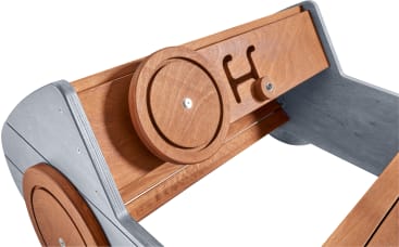 Nahaufnahme einer Holz- und Metallkonstruktion mit kreisförmigen und rechteckigen Holzpaneelen, mit einem ausgeschnittenen Buchstaben H im mittleren Paneel und sichtbaren Schrauben zur Befestigung der Komponenten.