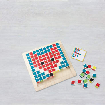 Ein Brettspiel aus Holz mit einem Gitter, das mit roten, blauen und weißen Spielsteinen gefüllt ist, die ein Muster bilden. Eine Referenzkarte mit demselben Muster und mehrere lose farbige Spielsteine werden neben dem Spielbrett auf einer hellen Fläche platziert.