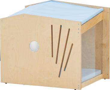 Ein hölzerner Kasten mit einem schrägen Dach, das mit hellblauem Stoff bespannt ist, einem runden Fenster, vertikalen Lamellen und einer offenen Seite mit einer durchsichtigen Platte, in der die Kinder spielen oder sich ausruhen können.