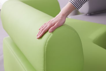 Die Hand einer Person ruht auf der Rückenlehne eines hellgrün gepolsterten Sofas. Nur der Arm und die Hand sind zu sehen. Die Person trägt ein langärmeliges, schwarz-weiß gestreiftes Hemd.