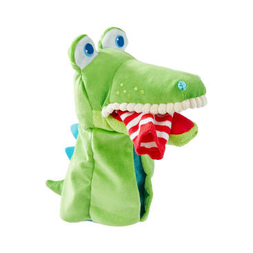 Eine grüne Plüsch-Alligatorpuppe mit blauen Augen und blauen Stacheln hält eine rot-weiß gestreifte Socke im Maul, dargestellt vor einem weißen Hintergrund.