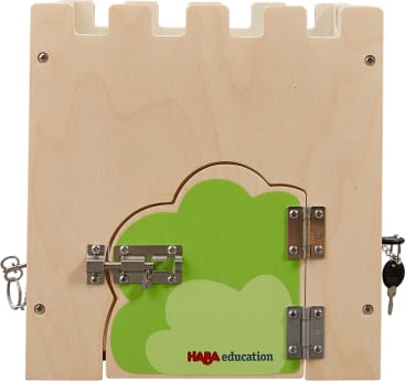 Ein hölzernes Spielbrett in Form einer Burgmauer mit grünem Buschmuster, mit Metallverschlüssen, Scharnieren, einem Schlüsselschloss und der Aufschrift "HABA education".