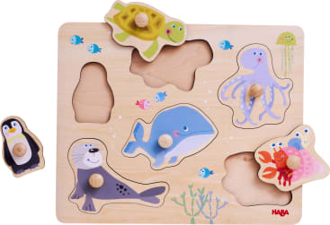 Ein Tierpuzzle aus Holz mit geformten Teilen, die eine Schildkröte, einen Pinguin, einen Wal, eine Robbe, einen Oktopus, eine Krabbe und einen Fisch darstellen. Einige Teile werden entfernt und außerhalb ihrer jeweiligen Schlitze platziert.