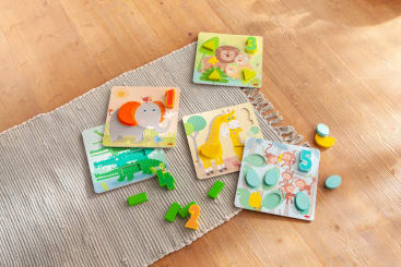 Vier bunte Holzpuzzlebretter mit Zahlen und passenden 3D-Teilen liegen auf einem beigen Teppich auf einem Holzboden. Die Zahlen 1, 2, 3 und 5 sind auf den Puzzlebrettern zu sehen.