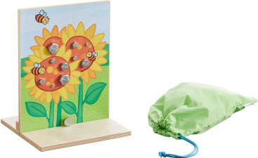 Ein Holzspielzeug mit einem Sonnenblumen- und Bienenmotiv und sechs sechseckigen Muttern, die in Löcher gesteckt sind. Es steht aufrecht auf einem Sockel. Rechts neben dem Spielzeug befindet sich ein hellgrüner Beutel mit Kordelzug.