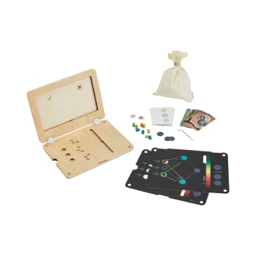 Ein hölzernes Spielbrett mit Deckel, illustrierte Karten, farbige Stifte, ein kleines Werkzeug und ein beigefarbener Beutel mit Kordelzug auf einer weißen Fläche.
