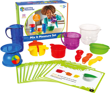Ein Misch- und Messset für Kinder mit bunten Bechern, Löffeln, einer Waage, Krügen und Aktivitätskarten, die vor der Produktverpackung ausgestellt sind. Das Set enthält 22 Teile für praktische Messaktivitäten.
