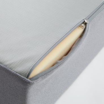 Nahaufnahme eines grauen Kissens oder einer grauen Matratze mit einem strukturierten Stoffbezug, der teilweise geöffnet wurde und eine Schicht gelben Schaumstoffs im Inneren offenbart.