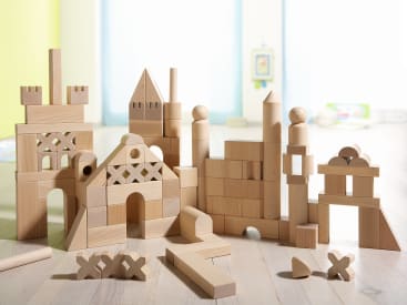 Verschiedene Holzbausteine werden auf einer hellen Oberfläche zu unterschiedlichen geometrischen Strukturen gestapelt, wobei der unscharfe Hintergrund eine helle Innenumgebung suggeriert.